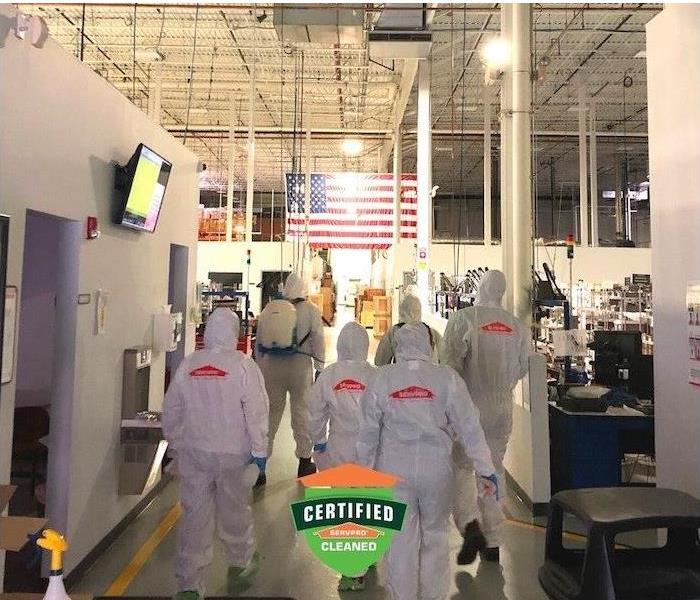 Photo shows a crew of SERVPRO employees in PPE gear walking inside commercial building