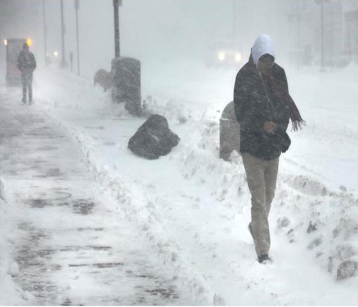 A man walks on a sidewalk during a winter storm